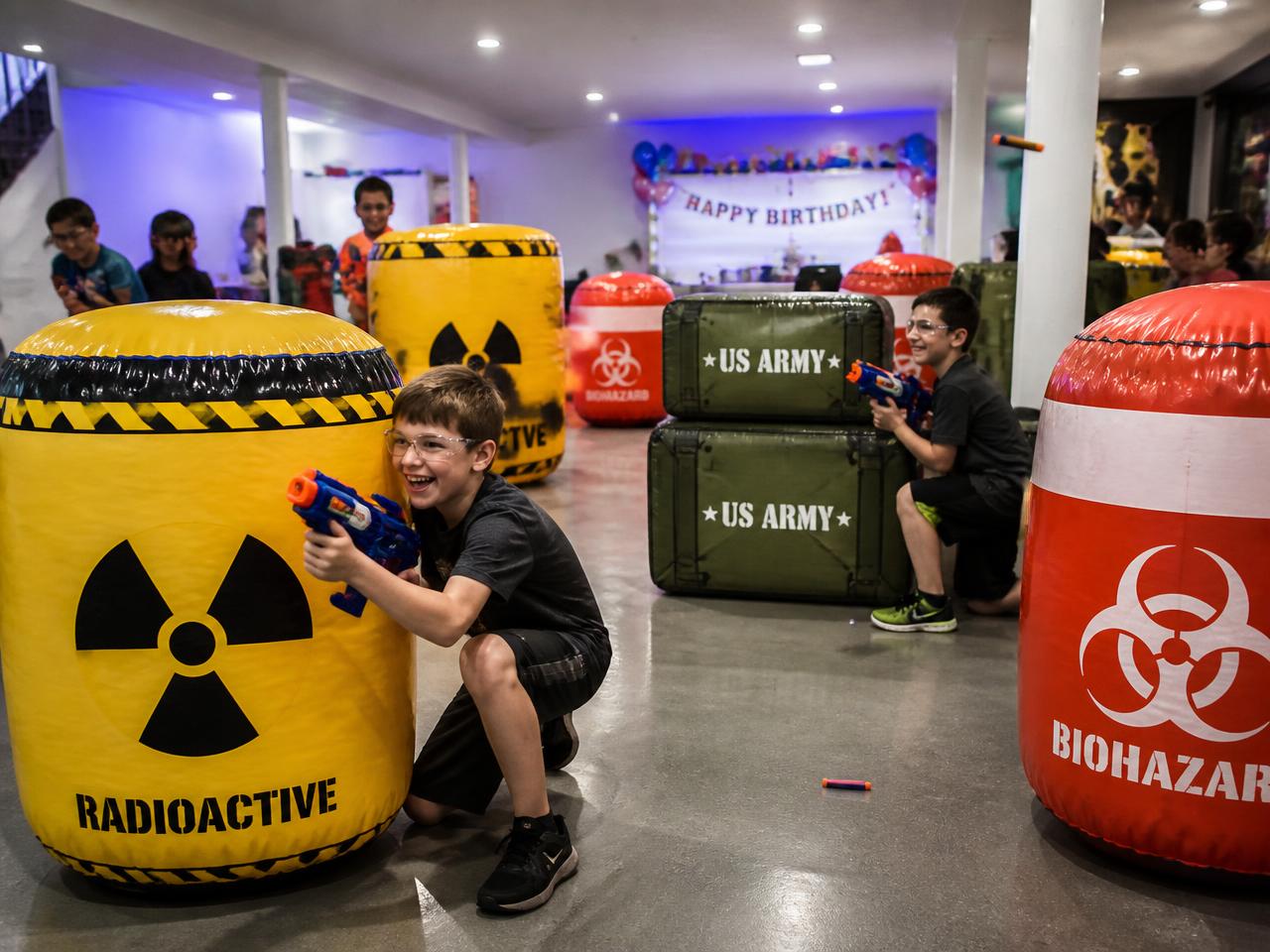 Indoor birthday foam dart battle with inflatable barricades in a basement party space